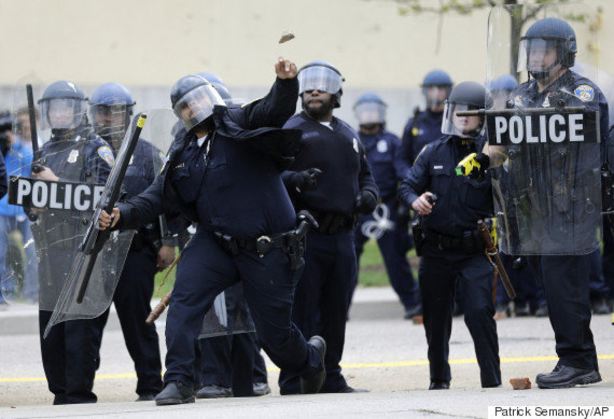 A police officer throws an object at protestors, Monday, April 27, 2015, following the funeral of Freddie Gray in Baltimore. Gray died from spinal injuries about a week after he was arrested and transported in a Baltimore Police Department van. (AP Photo/Patrick Semansky)