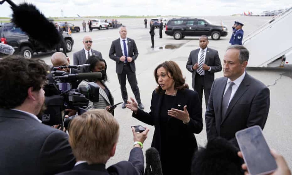 harris gestures while her husband, doug emhoff, looks on. a circle of reporters surround her